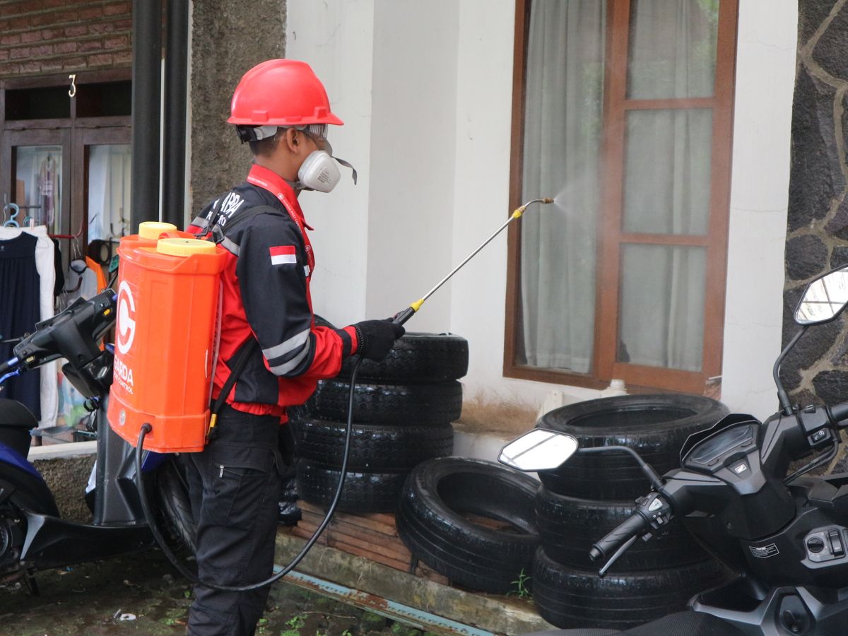 Técnico de fumigación con aspersora aplicando producto en el exterior de una casa